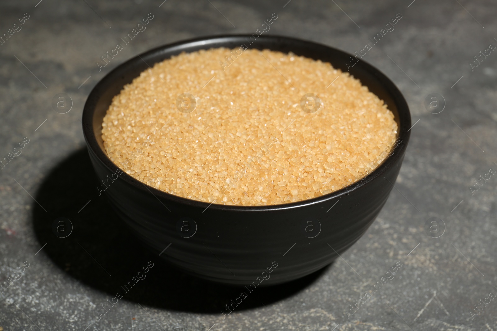 Photo of Brown sugar in bowl on grey textured table, closeup