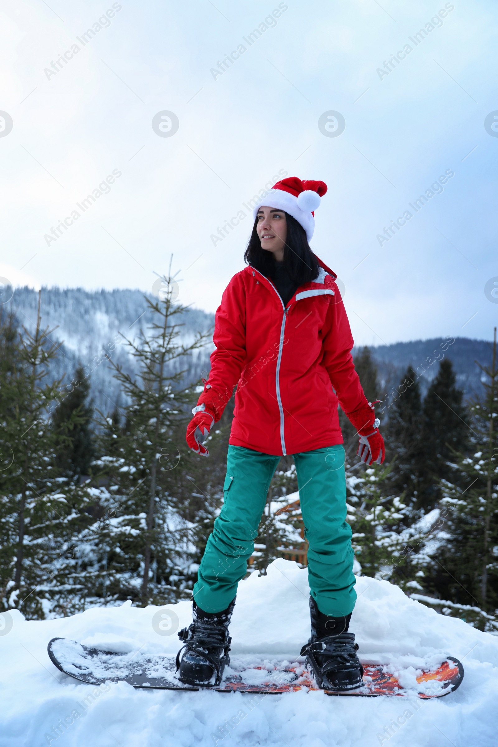 Photo of Young snowboarder wearing Santa hat on snowy hill. Winter vacation