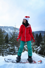 Photo of Young snowboarder wearing Santa hat on snowy hill. Winter vacation