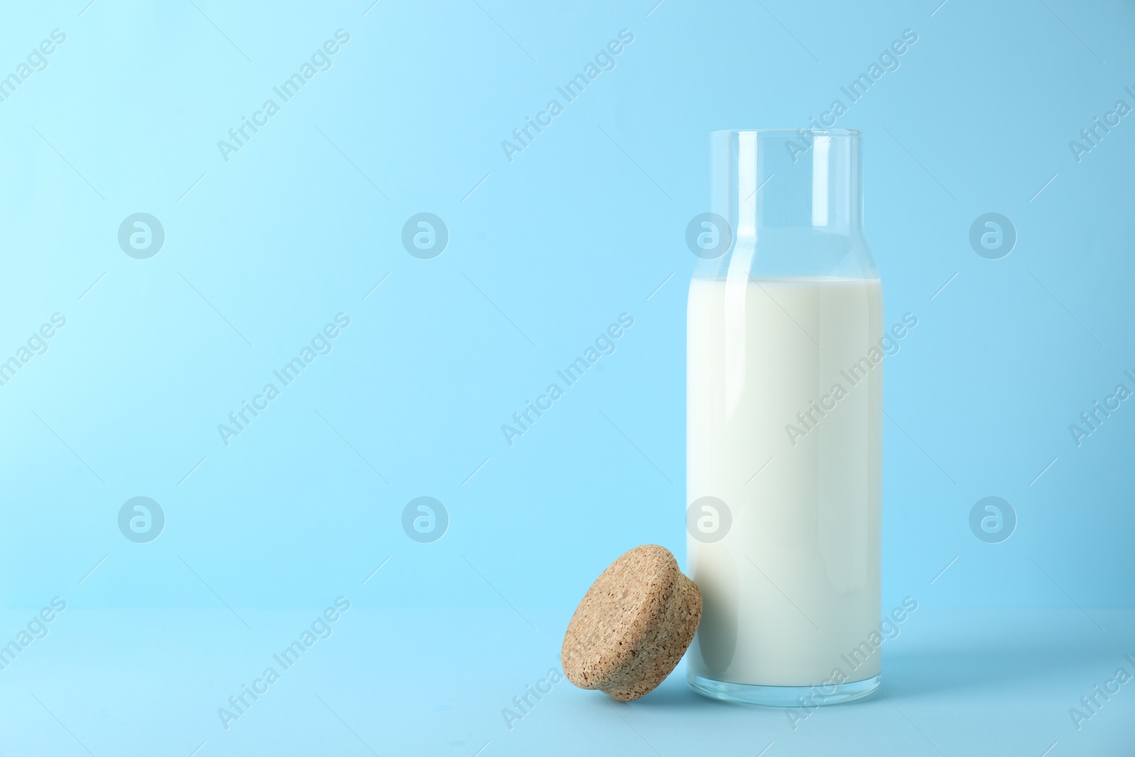 Photo of Glass carafe of fresh milk and lid on light blue background, space for text