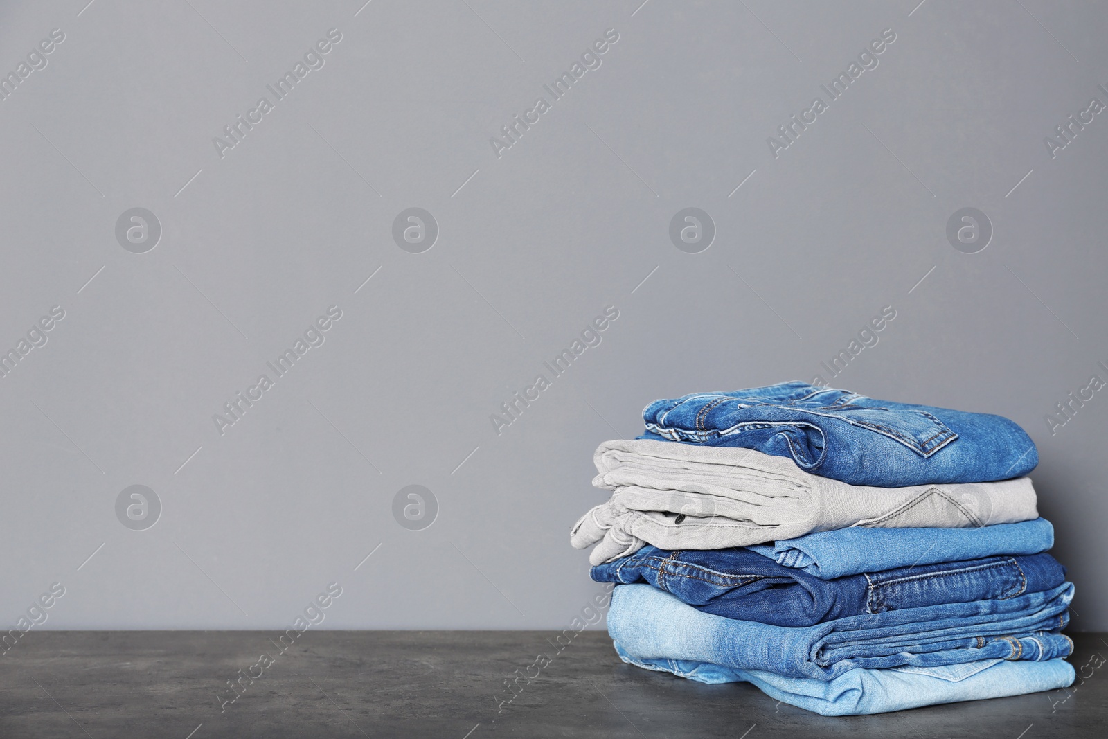 Photo of Stack of different jeans on  table against gray background. Space for text