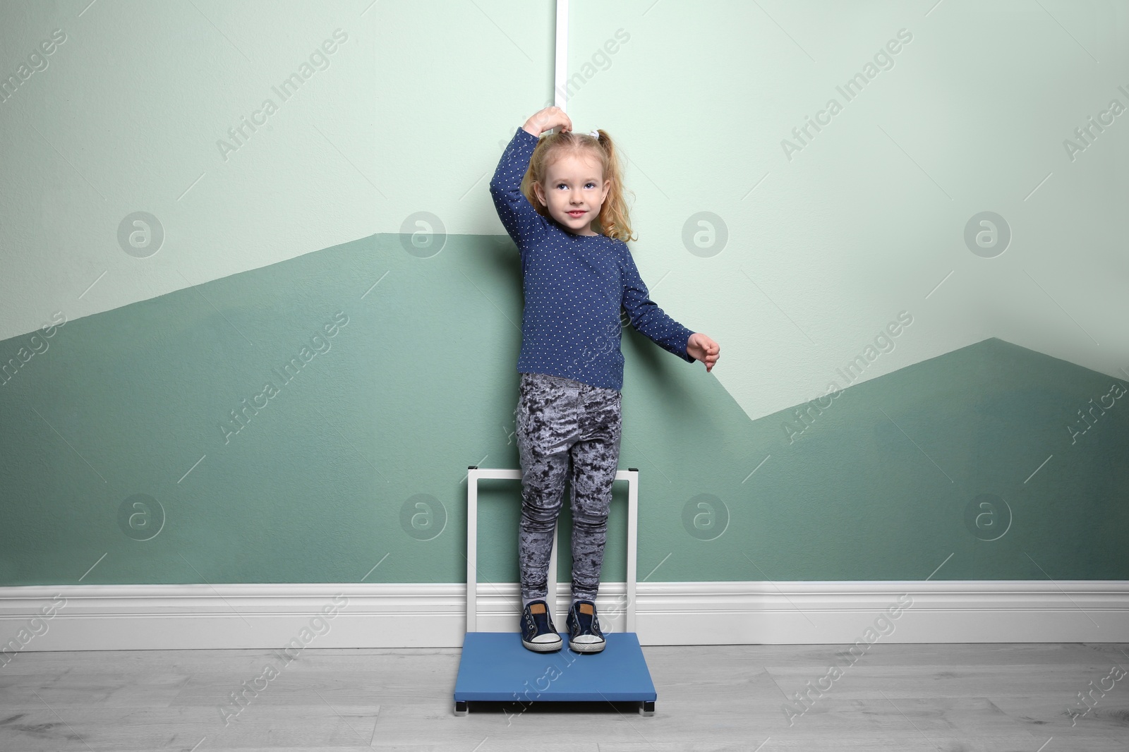 Photo of Little girl measuring her height near color wall