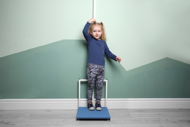 Little girl measuring her height near color wall