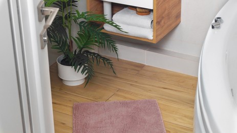 Photo of Soft bath mat near houseplant on wooden floor in bathroom