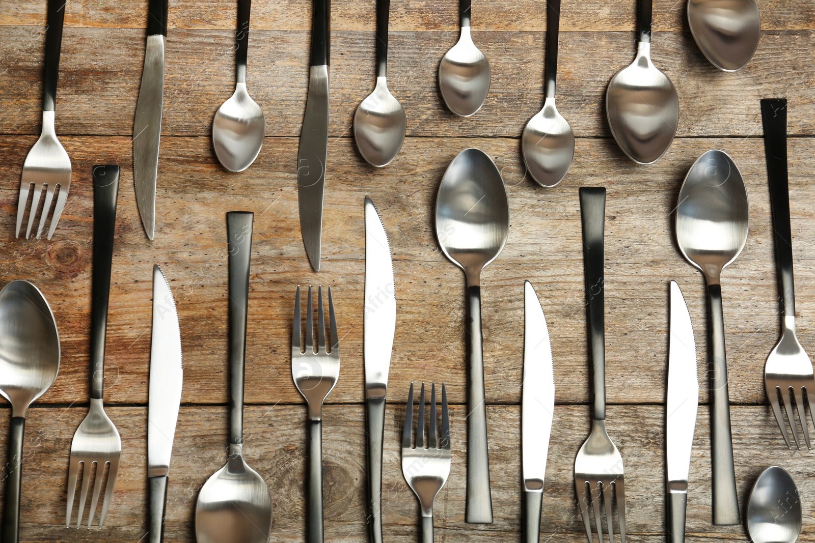 Photo of Forks, knives and spoons on wooden table, top view