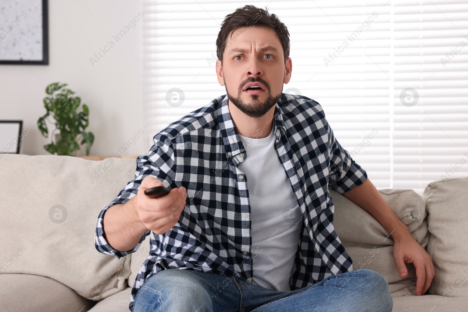 Photo of Emotional man with remote controller watching TV at home