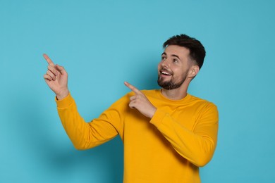 Photo of Handsome man in yellow sweatshirt pointing at something on light blue background