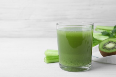 Glass of fresh celery juice on white wooden table, space for text