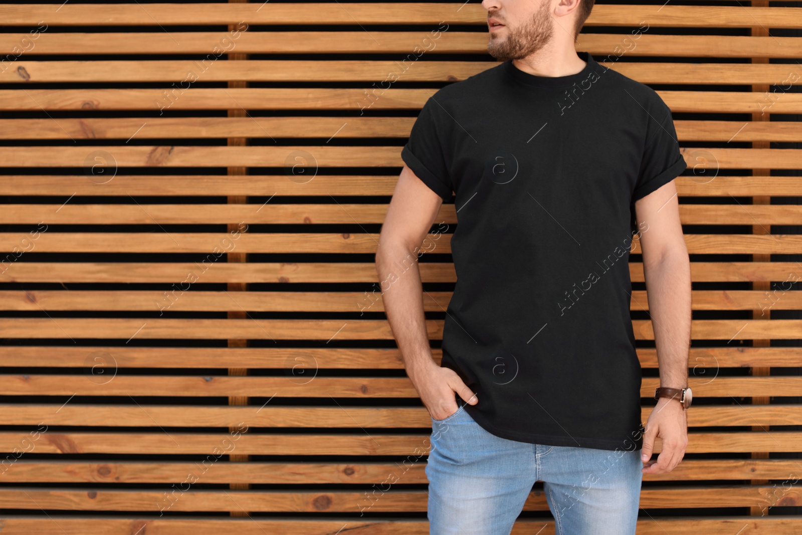 Photo of Young man wearing black t-shirt against wooden wall on street. Urban style