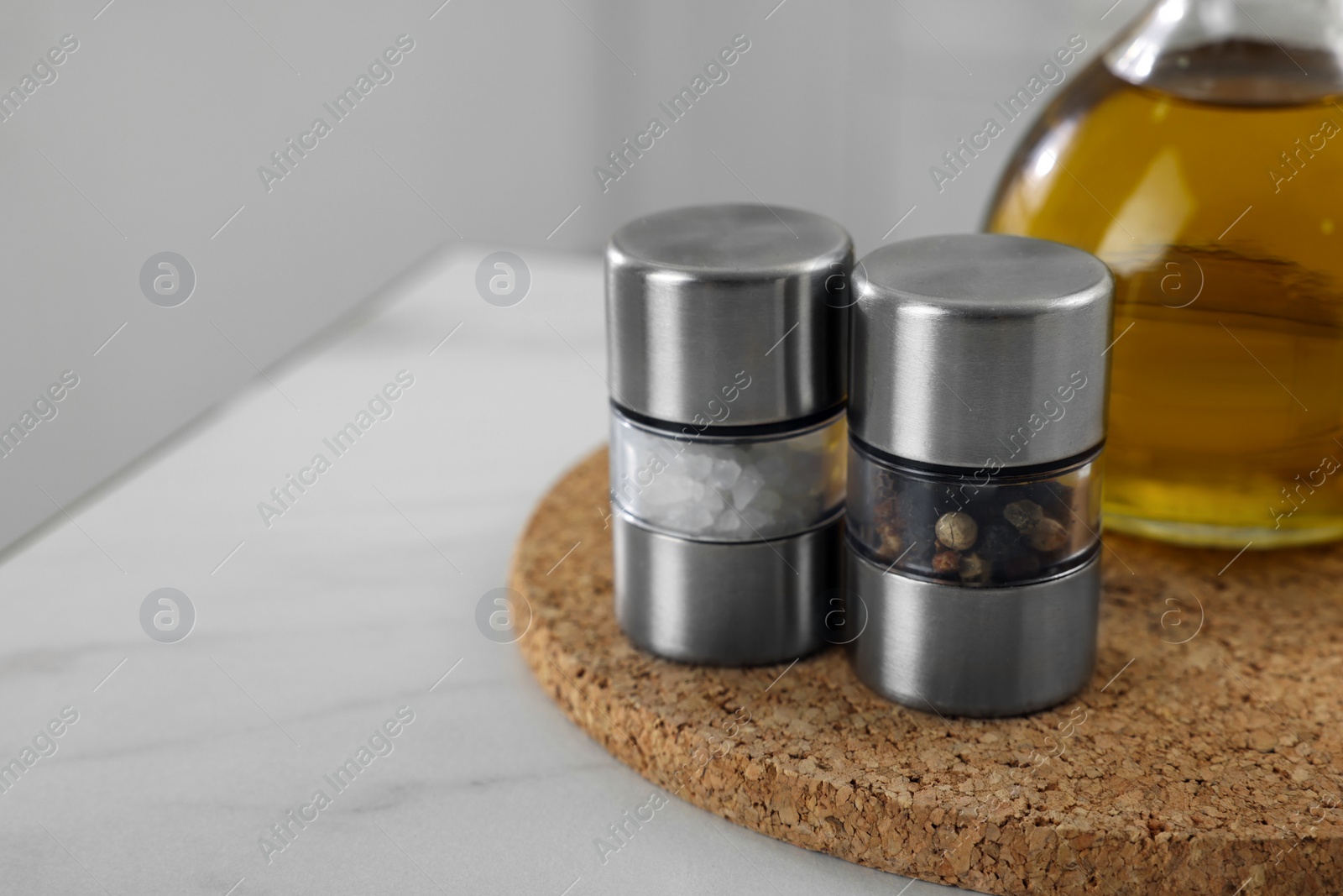 Photo of Salt and pepper mills with bottle of oil on white marble table, closeup. Space for text