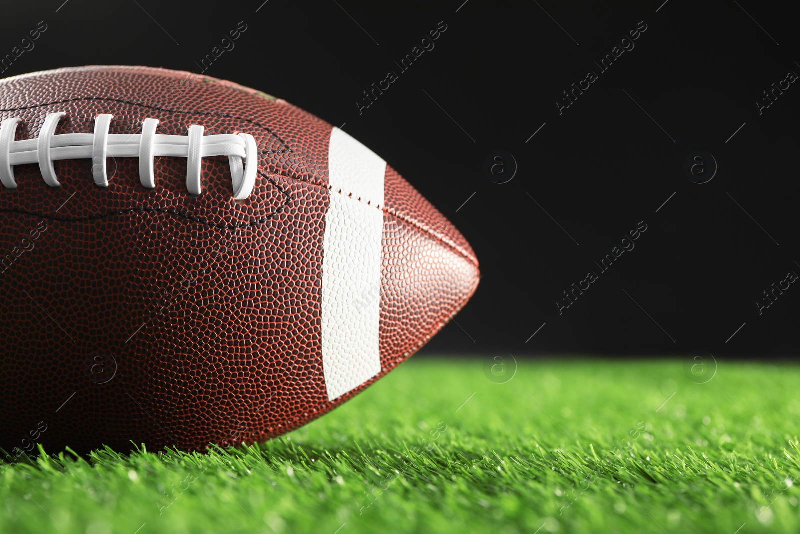 Photo of Rugby ball on green grass against black background, closeup. Space for text