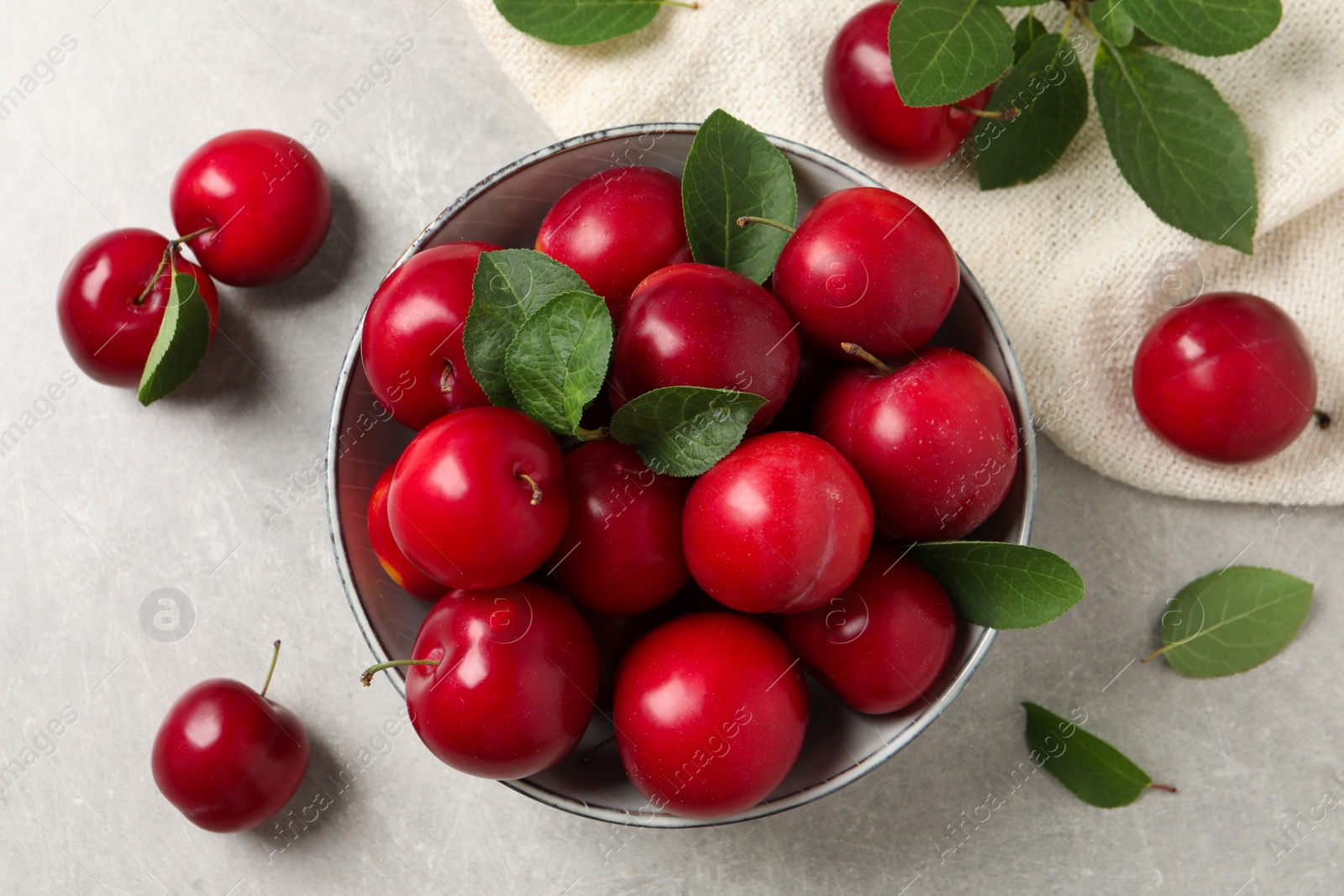 Photo of Delicious ripe cherry plums with leaves on light table, flat lay