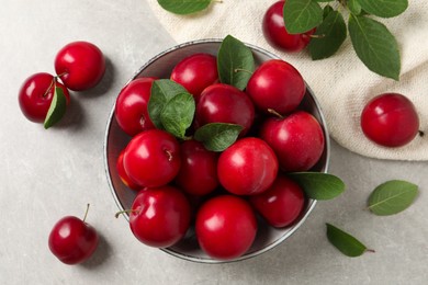 Photo of Delicious ripe cherry plums with leaves on light table, flat lay