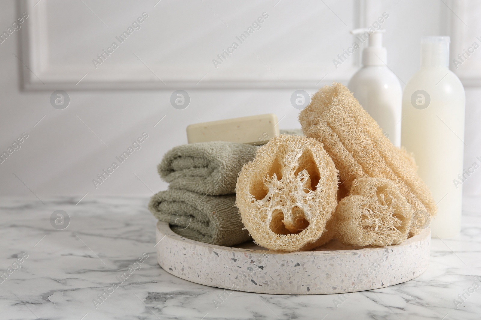 Photo of Loofah sponges, towels, soap and cosmetic products on white marble table, space for text