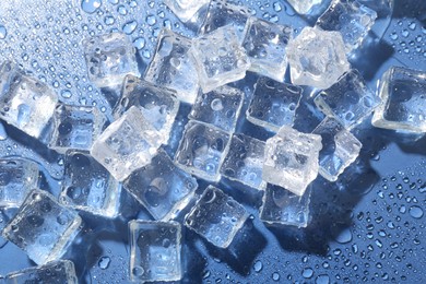 Melting ice cubes and water drops on blue background, flat lay