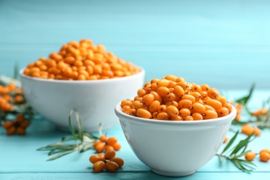 Photo of Fresh ripe sea buckthorn in bowl on light blue wooden table