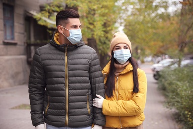 Photo of Couple in medical face masks and gloves walking outdoors. Personal protection during COVID-19 pandemic