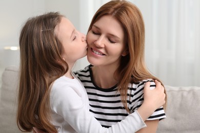 Photo of Cute daughter kissing her mom on sofa at home