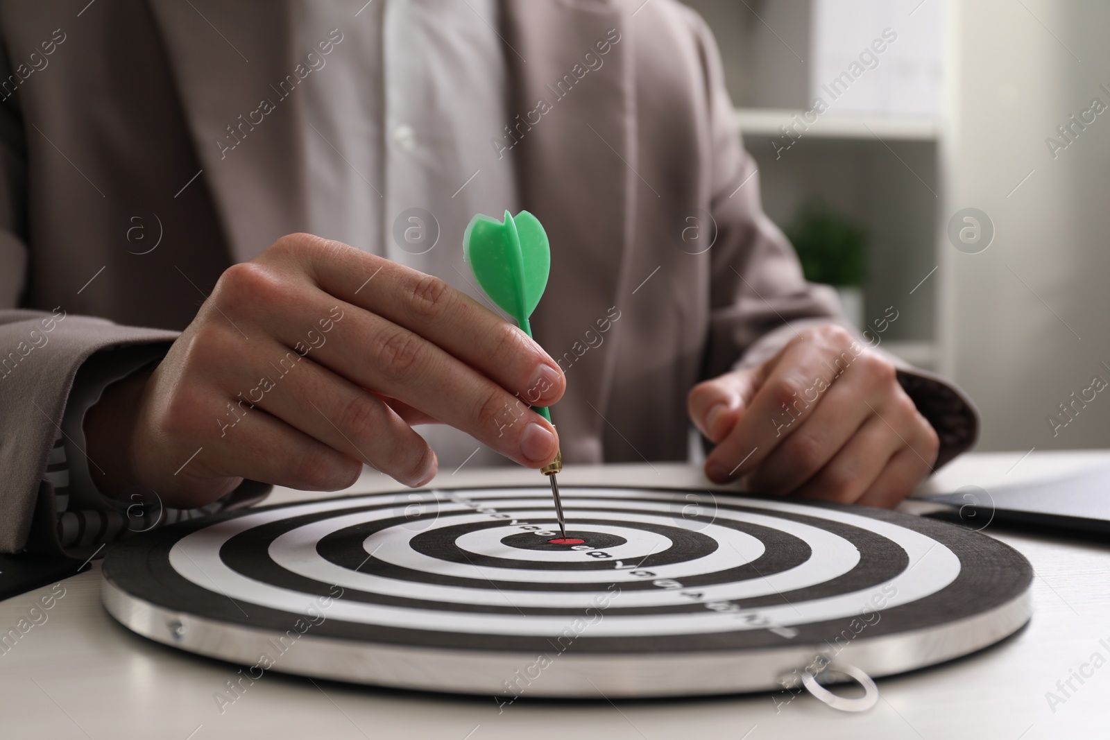 Photo of Business targeting concept. Man with dart aiming at dartboard at table indoors, closeup