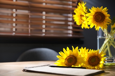 Bouquet of beautiful sunflowers and notebook on wooden table in room. Space for text