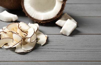 Photo of Pile of tasty coconut chips on grey wooden table. Space for text
