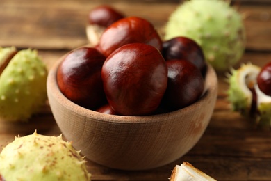 Photo of Horse chestnuts in bowl on wooden table, closeup