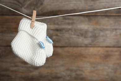 Photo of Pair of knitted booties on laundry line against wooden background, space for text. Baby accessories