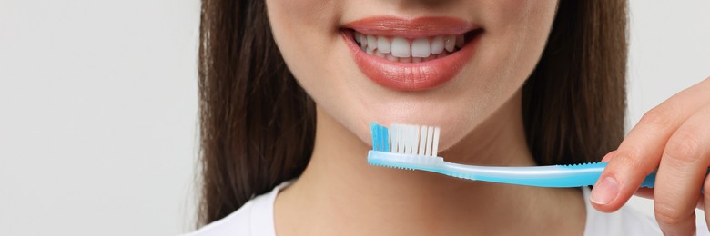 Woman holding plastic toothbrush on white background, closeup. Banner design with space for text