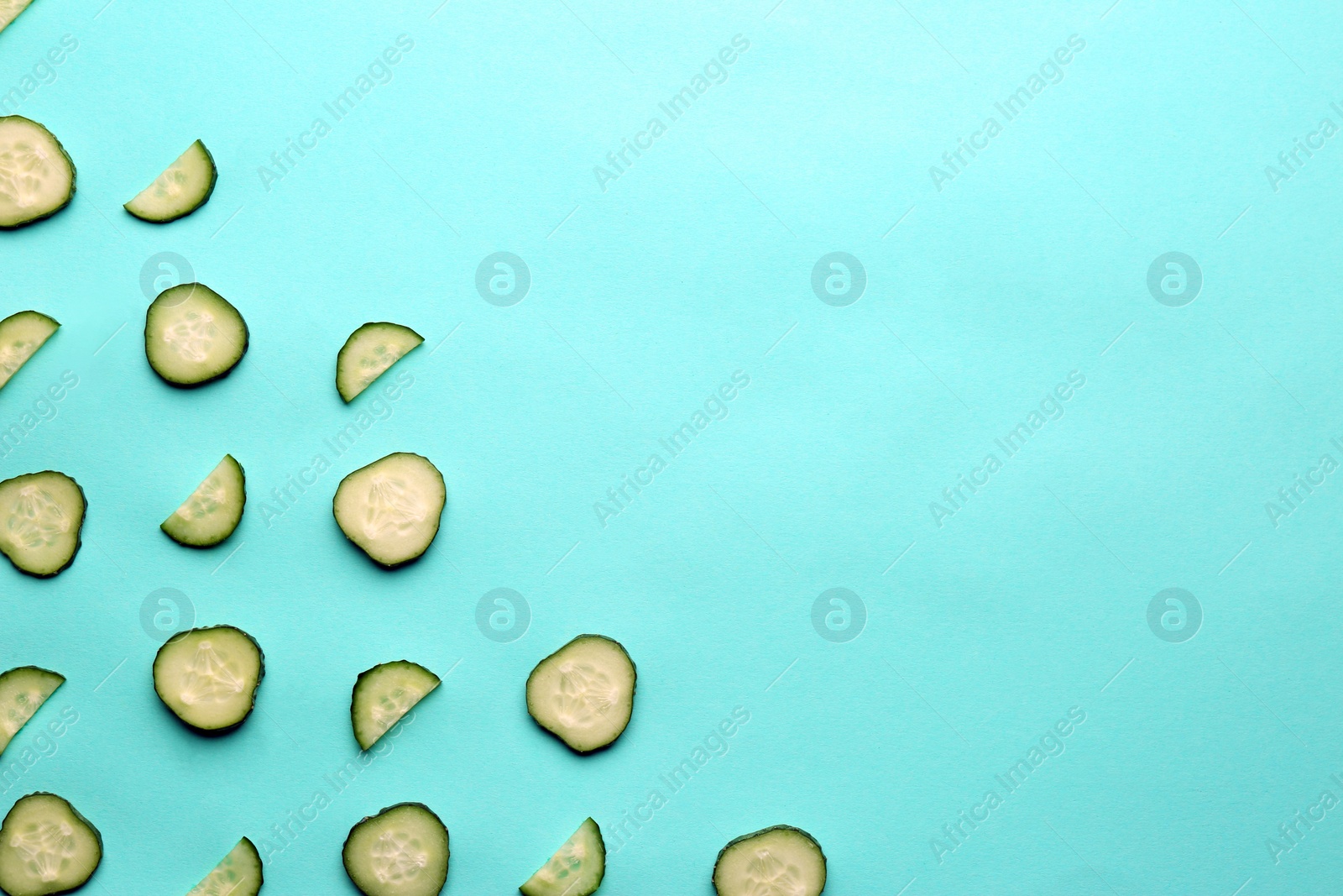 Photo of Slices of fresh ripe cucumber on turquoise background, flat lay. Space for text