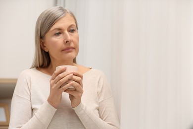 Photo of Menopause, mood changes. Sad woman with cup of drink at home, space for text