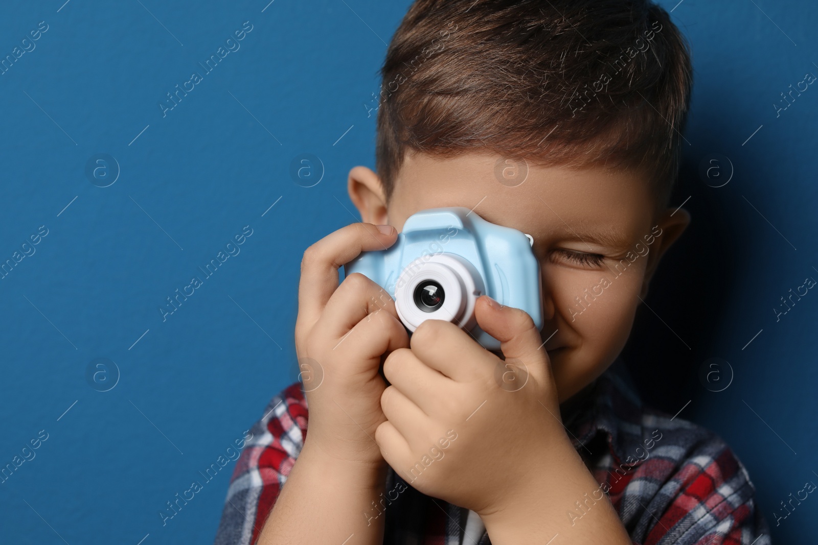 Photo of Little photographer taking picture with toy camera on blue background