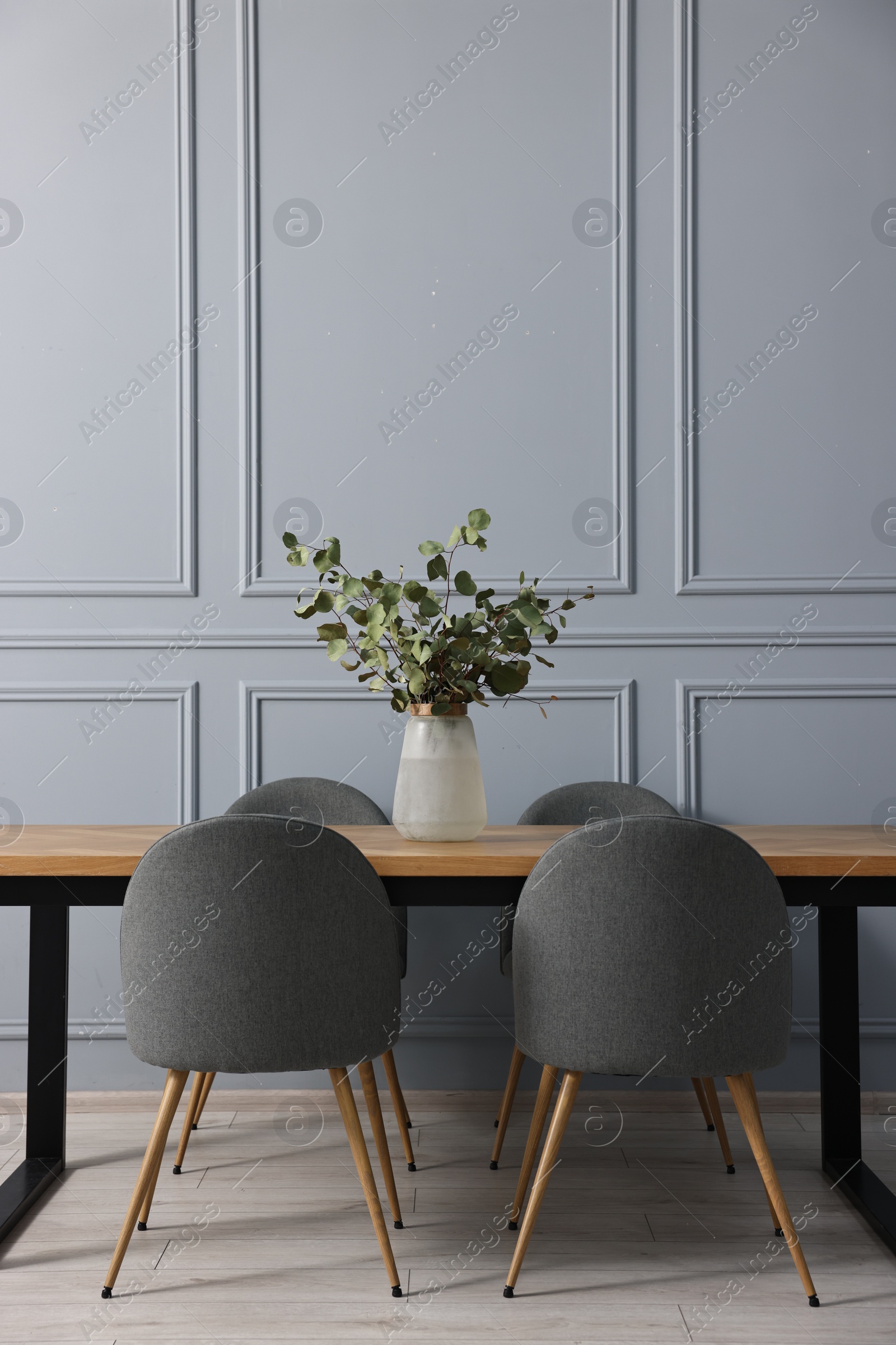 Photo of Soft chairs, table and vase with eucalyptus branches in stylish dining room