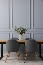 Soft chairs, table and vase with eucalyptus branches in stylish dining room