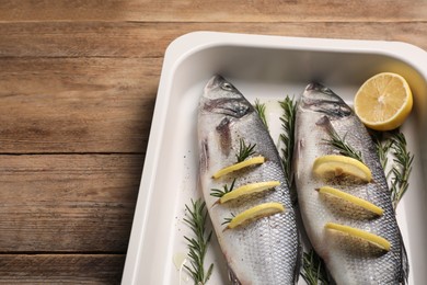 Baking tray with raw sea bass fish, lemon and rosemary on wooden table, closeup