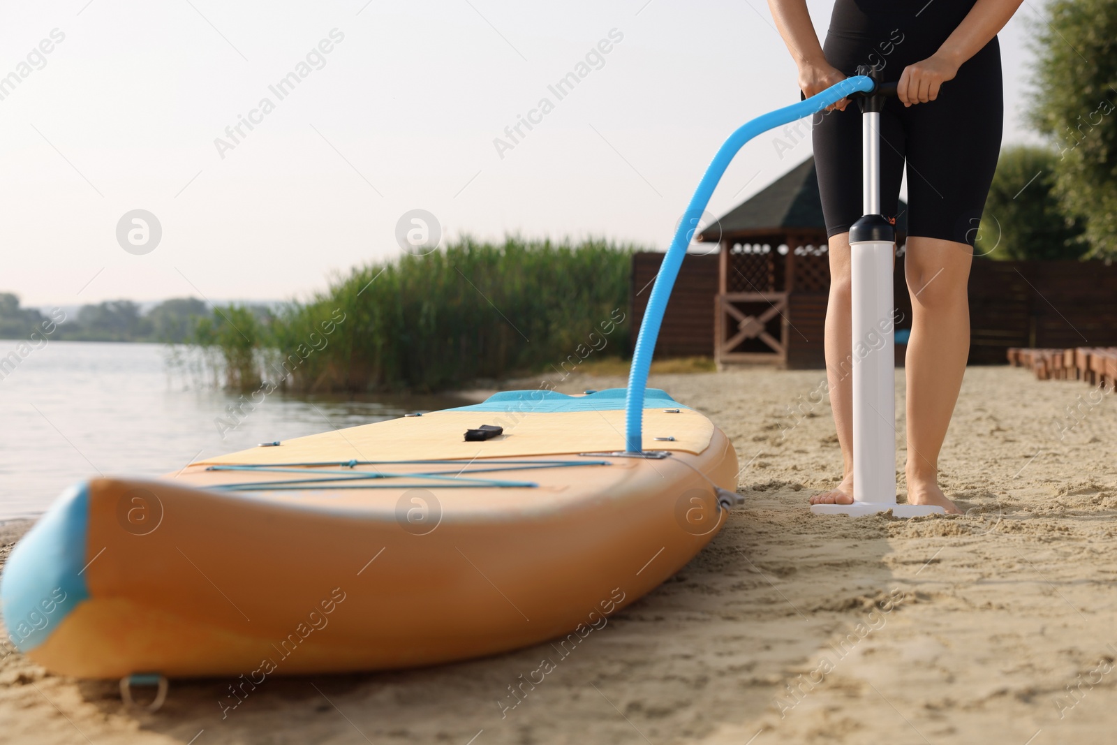 Photo of Woman pumping up SUP board on river shore, closeup