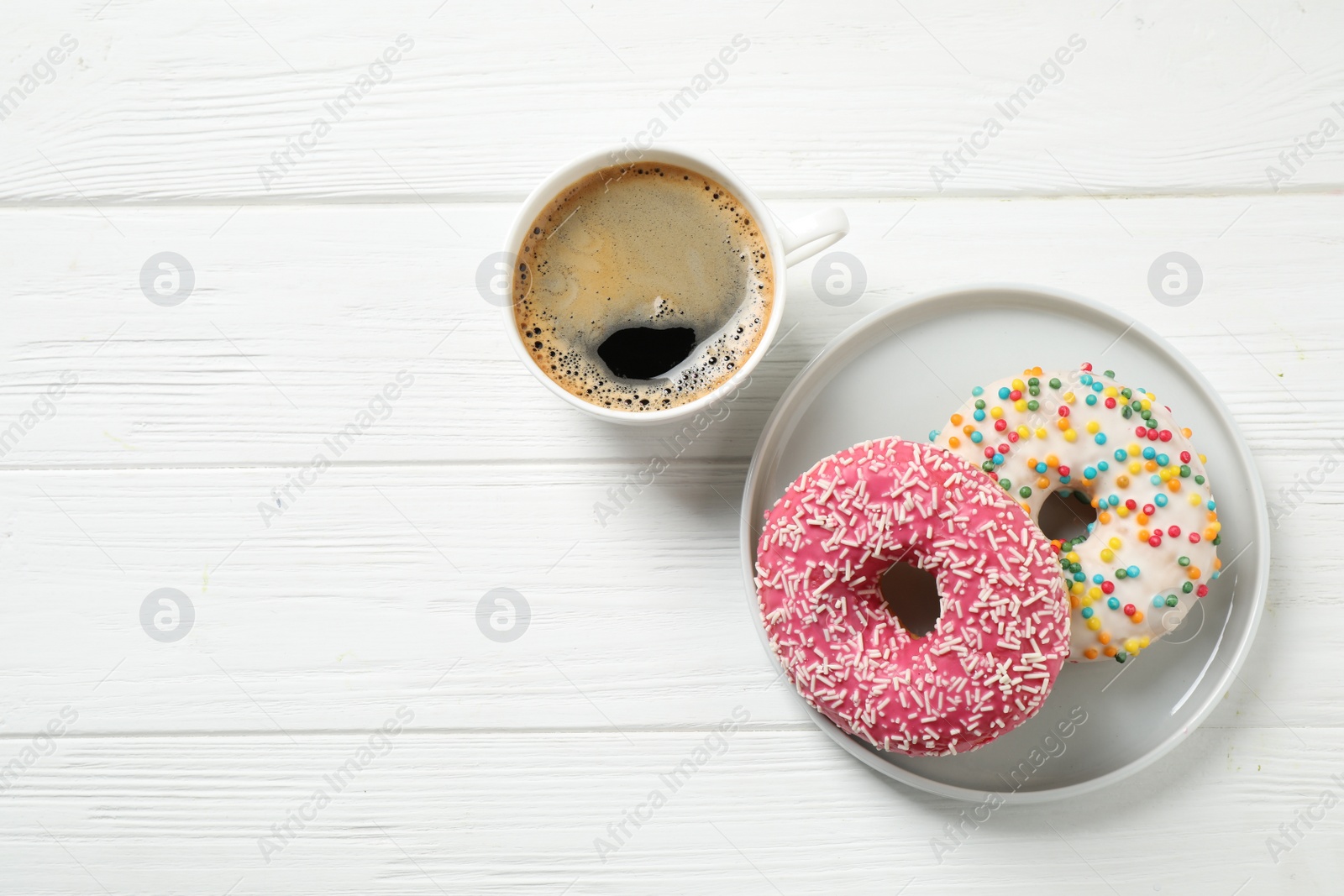 Photo of Yummy donuts with sprinkles and coffee on white wooden table, flat lay. Space for text