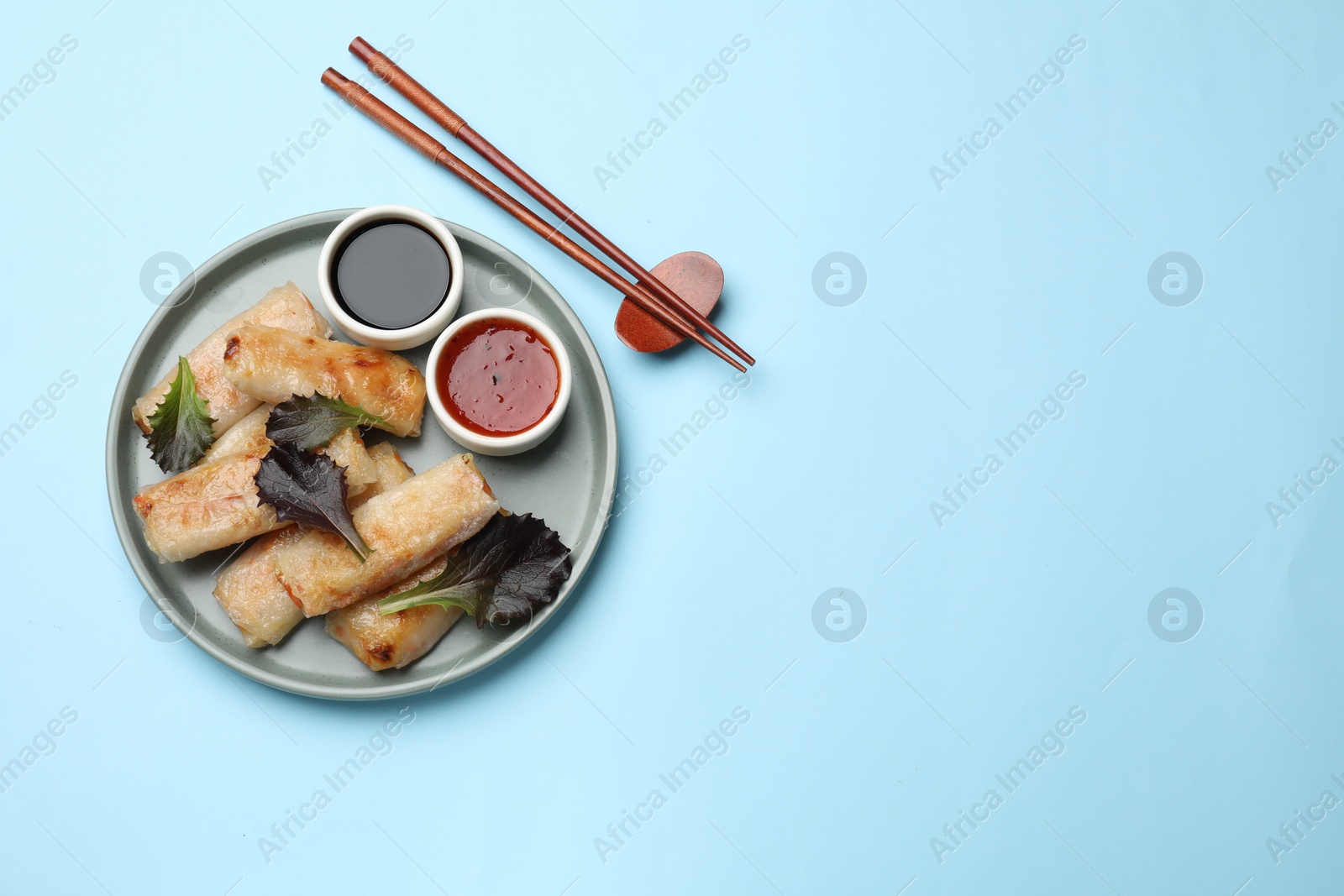 Photo of Tasty fried spring rolls, lettuce and sauces served on light blue table, top view. Space for text