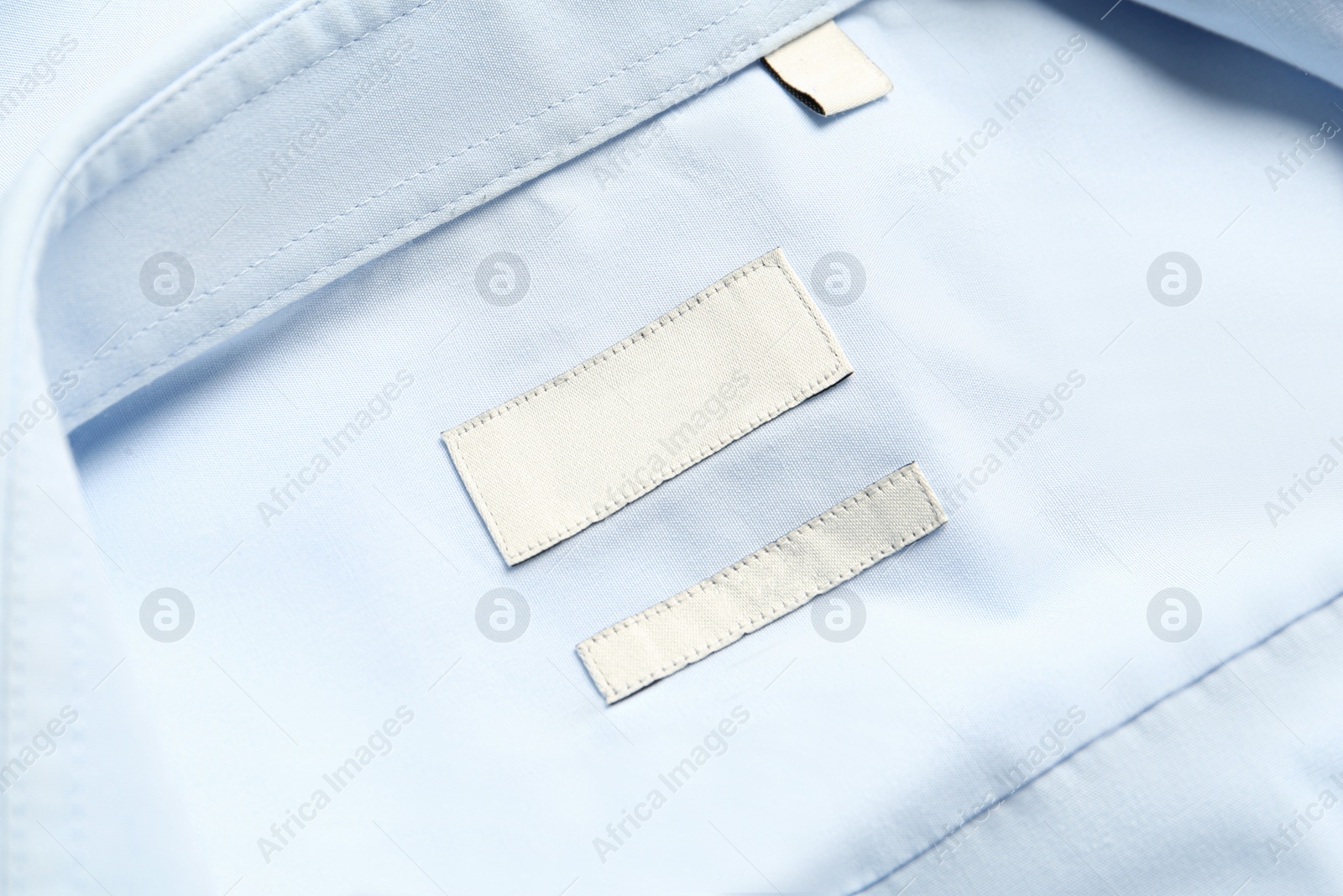 Photo of Blank clothing labels on light blue shirt, top view