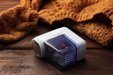 Photo of Modern fabric shaver with fuzz and orange knitted sweater on wooden table, closeup