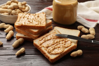 Photo of Delicious toasts with peanut butter, nuts and knife on dark wooden table