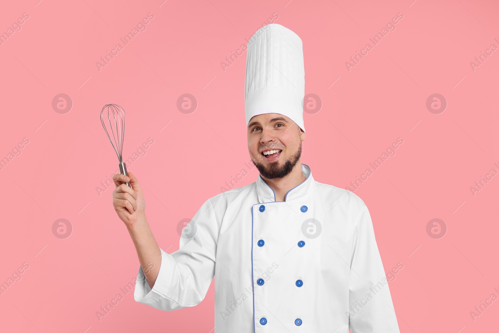 Photo of Happy professional confectioner in uniform holding whisk on pink background