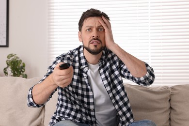 Photo of Emotional man with remote controller watching TV at home