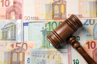 Photo of Tax law. Wooden gavel on euro banknotes, top view