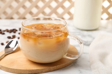 Photo of Refreshing iced coffee with milk in glass cup and spoon on white table, closeup