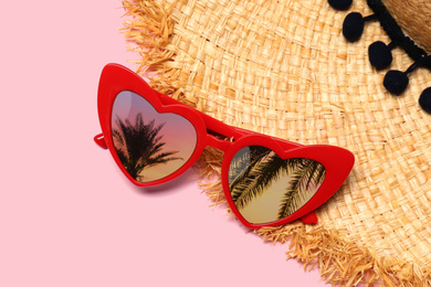 Image of Heart shaped sunglasses with reflection of palm trees on pink background, flat lay 