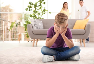 Photo of Upset child sitting on floor while parents fighting on background. Family relationships