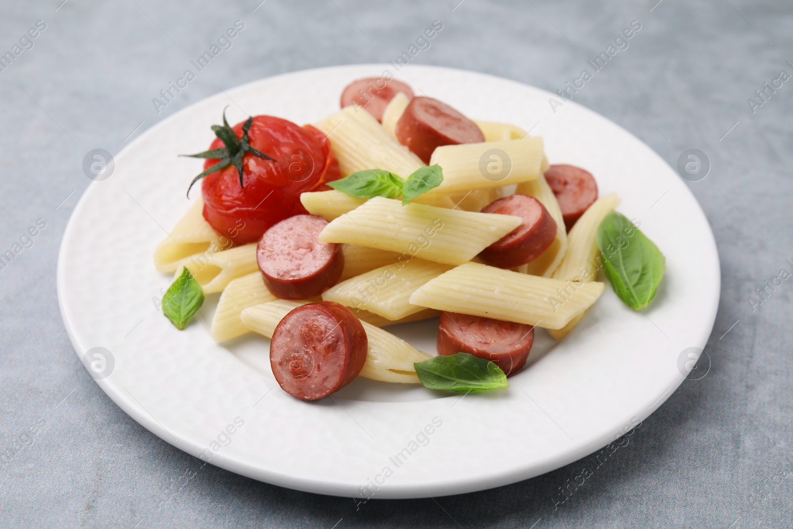 Photo of Tasty pasta with smoked sausage, tomato and basil on light grey table, closeup