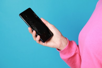 Photo of Woman holding damaged smartphone on light blue background, closeup. Device repairing