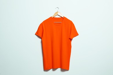 Hanger with orange t-shirt on light wall. Mockup for design