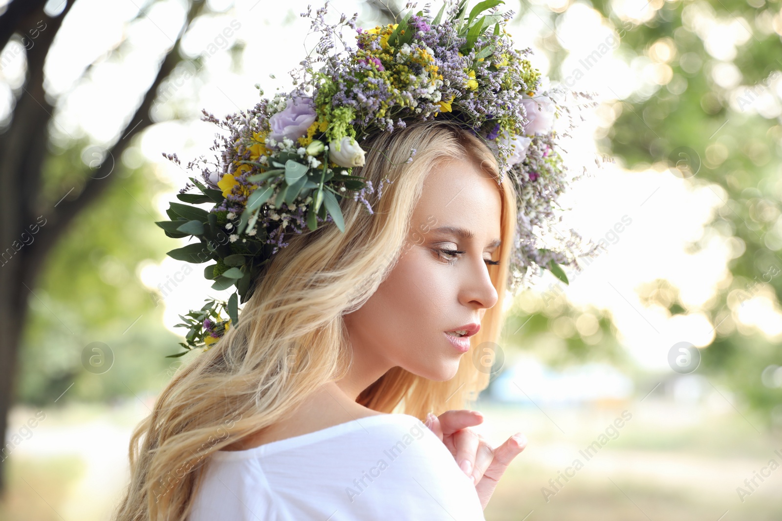 Photo of Young woman wearing wreath made of beautiful flowers outdoors on sunny day